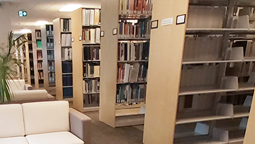 Several rows of bookshelves stretch back alongside some chairs in the CER library