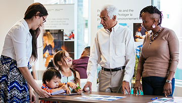 An Indigenous mother with her two children talking with a CER employee at an open information session