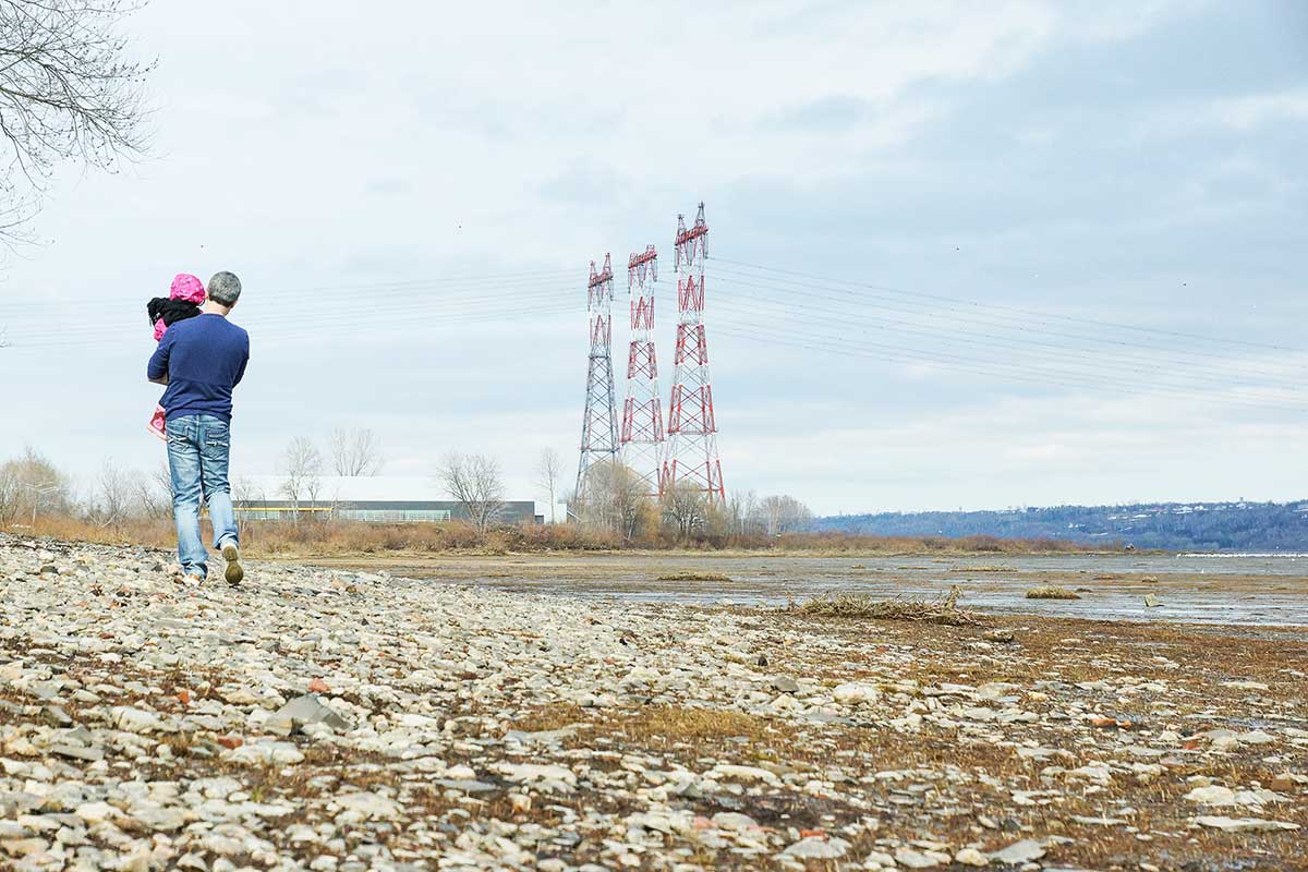 Figure 1 – Sur la berge d’une voie navigable, un homme marche avec un enfant vers trois pylônes électriques.