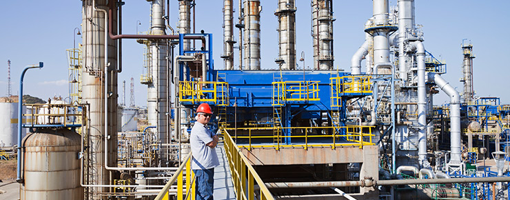 Travailleur portant un casque rouge sur un pont d’accès à une raffinerie 