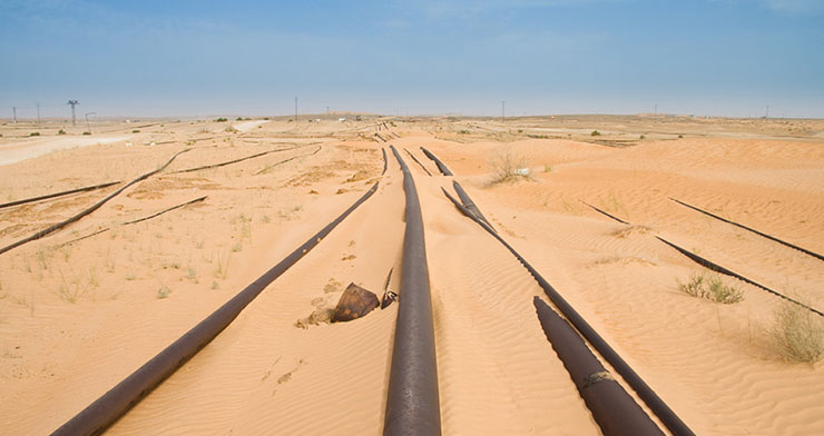 Pipelines partially covered by sand in the desert and power lines on the horizon