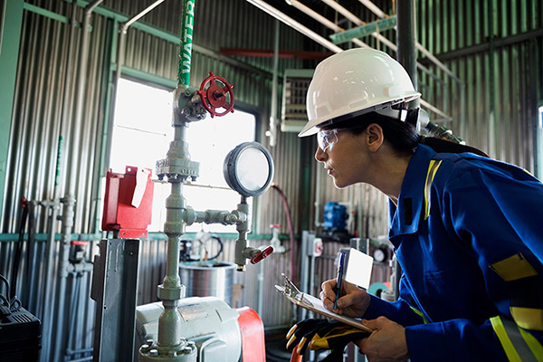 Ingénieur avec équipement de protection individuelle inspectant une vanne de distribution de pression dans une usine à gaz
