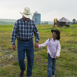 Grand-père et petite-fille avec chapeaux de cow boy marchant dans un champ en se tenant la main.