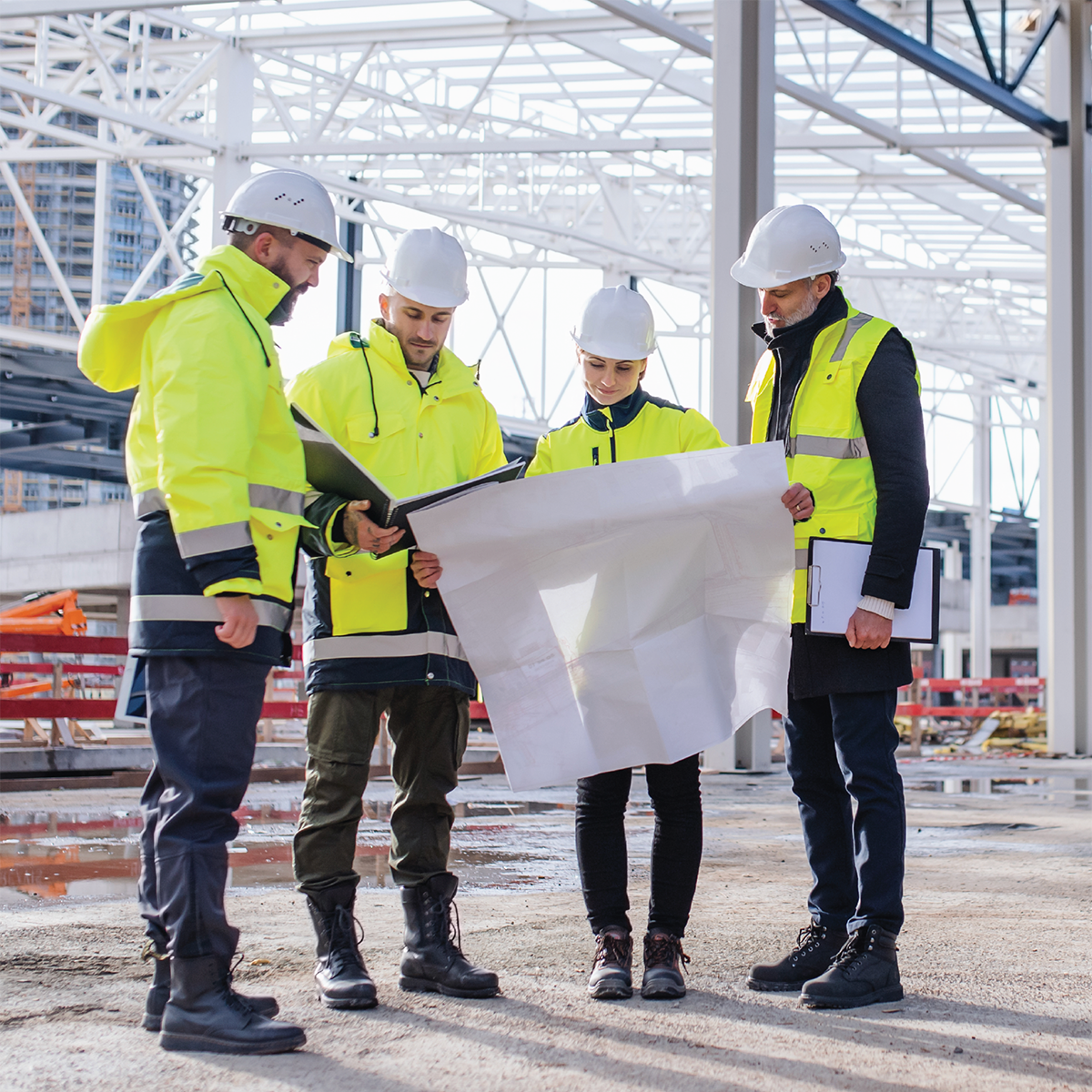 Group of engineers with blueprints standing on construction site
