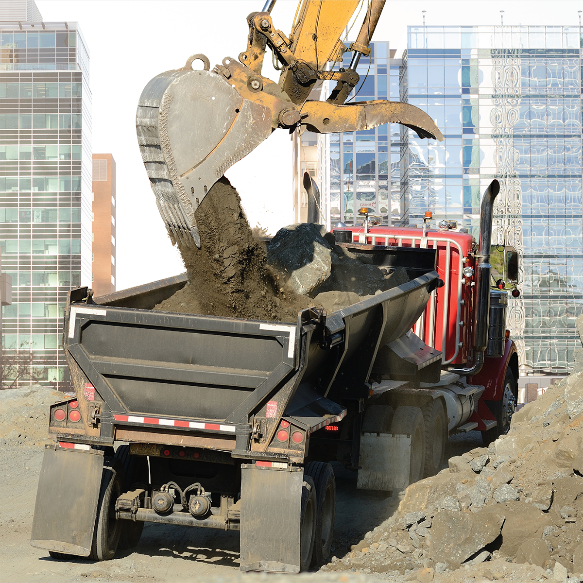 Shovel loading dirt into dump truck with office buildings in background