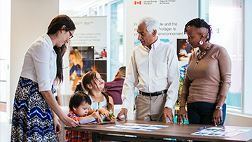 An Indigenous mother with her two children talking with a CER employee at an open information session