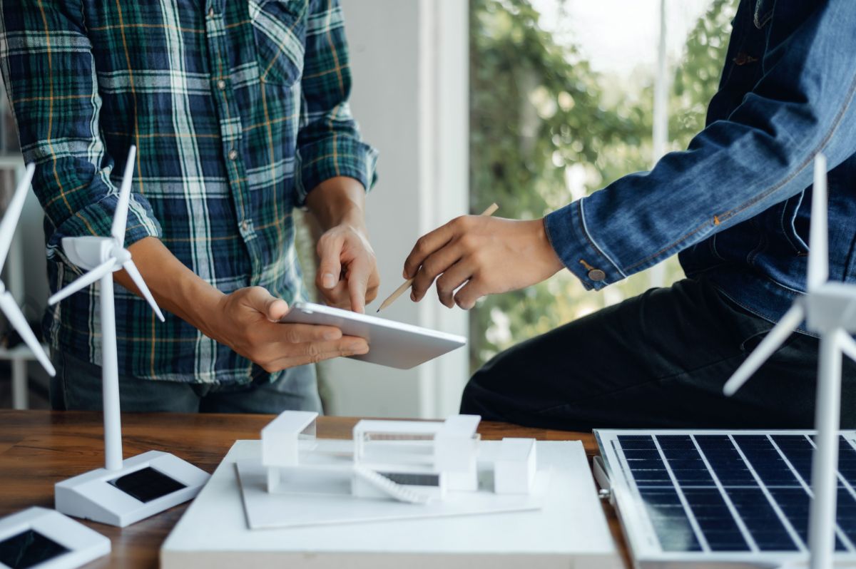 Mains d’un technicien travaillant sur une tablette avec des modèles d’éoliennes.