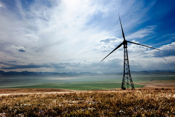 A wind turbine in a field with partially cloudy skies, mountain range in the distance