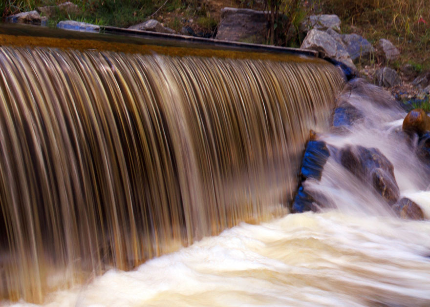 Detailed view of water flowing over a dam and river rocks