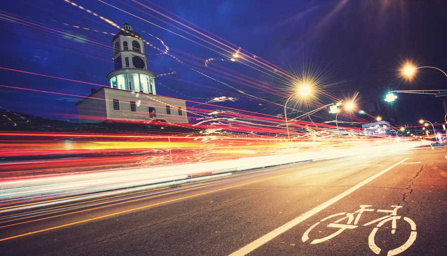 Traits lumineux laissés par les phares de voitures qui éclairent une piste cyclable le soir au centre de Halifax