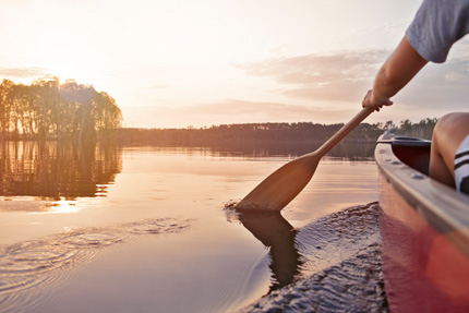Detail of a canoer paddling through a lake at dusk