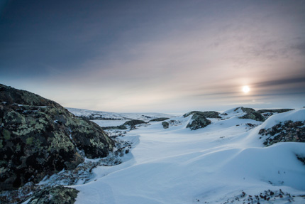 Snow covered mountain tops recede into the horizon as the sun sets