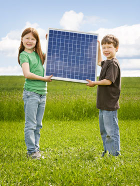 Deux enfants, un garçon et une fille, qui tiennent un panneau solaire dans un champ d’herbes
