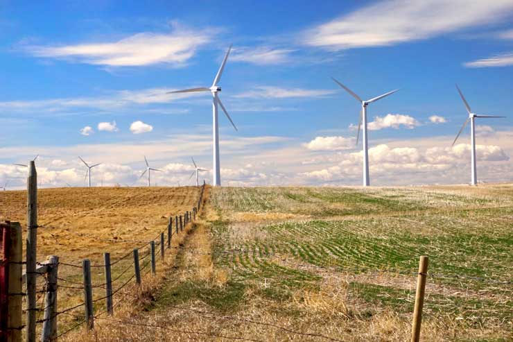 Wind turbines in a farmers field, old fence posts run adjacent, under a partly cloudy sky