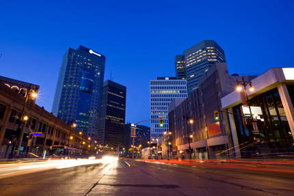 Centre de Winnipeg la nuit alors que les voitures qui circulent illuminent la voie.