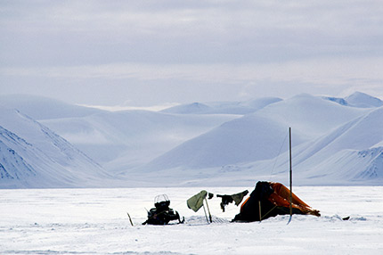 An Inuit woman carries her infant on her back as they traverse the snowy tundra