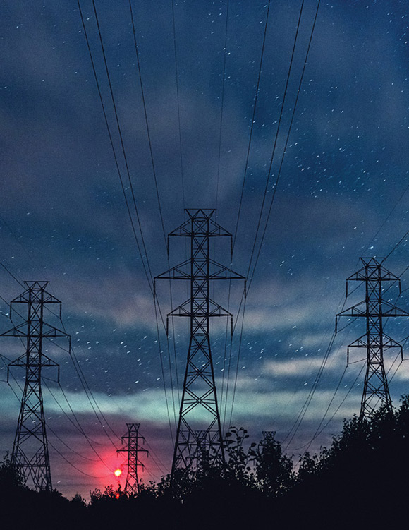 Lignes de transport d’électricité sous un ciel étoilé avec phare d’un pylône de transmission de téléphonie cellulaire au loin