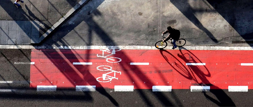 An aerial view of a cyclist riding their bicycle on a red painted cycle track at dusk.
