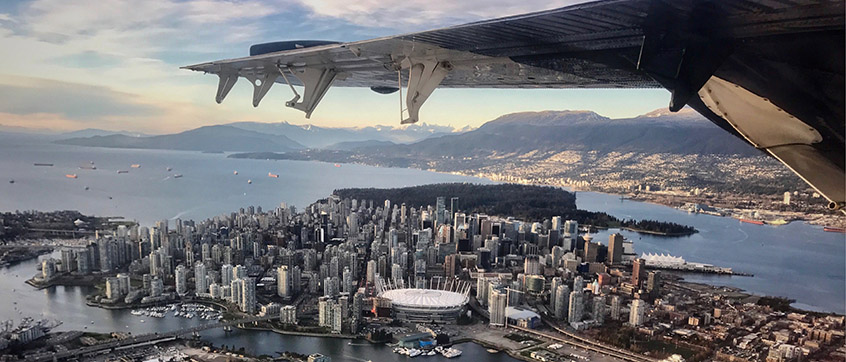Aile d’un avion survolant Vancouver. Ville, océan et montagnes vus du ciel.