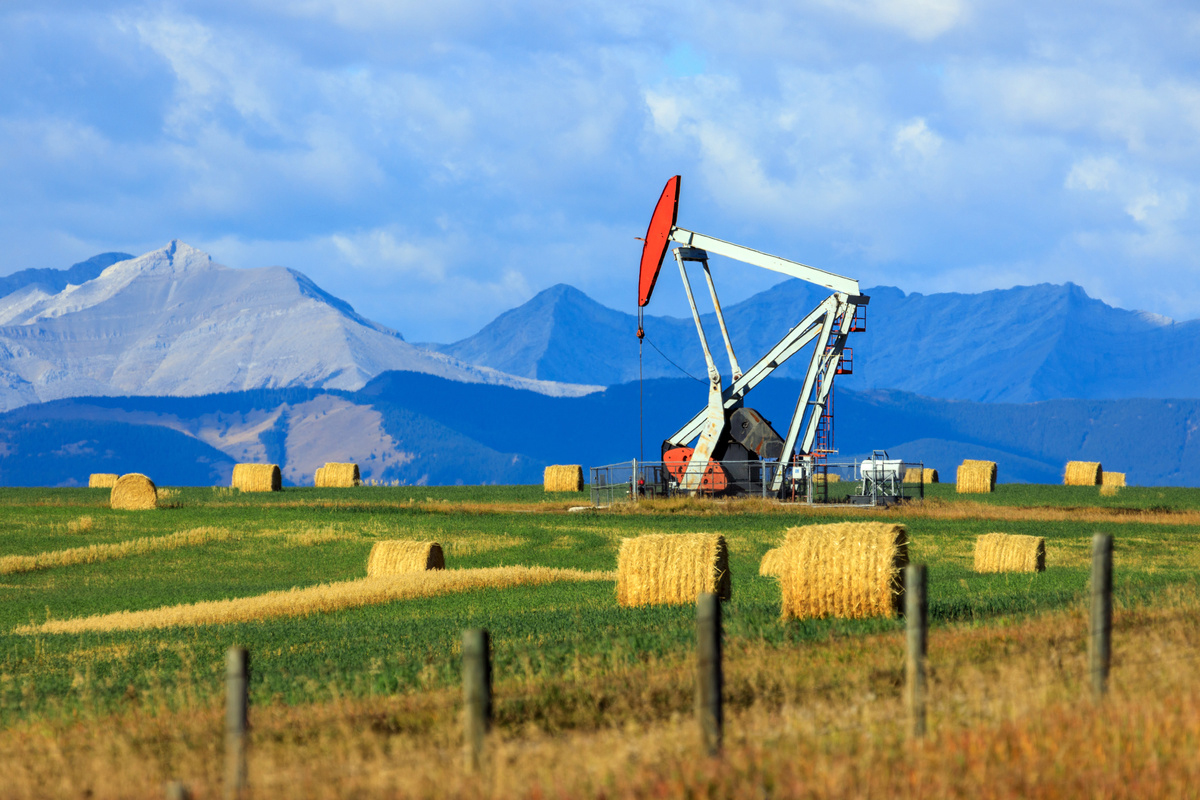 Oil derrick in an Alberta field with mountains in the background.