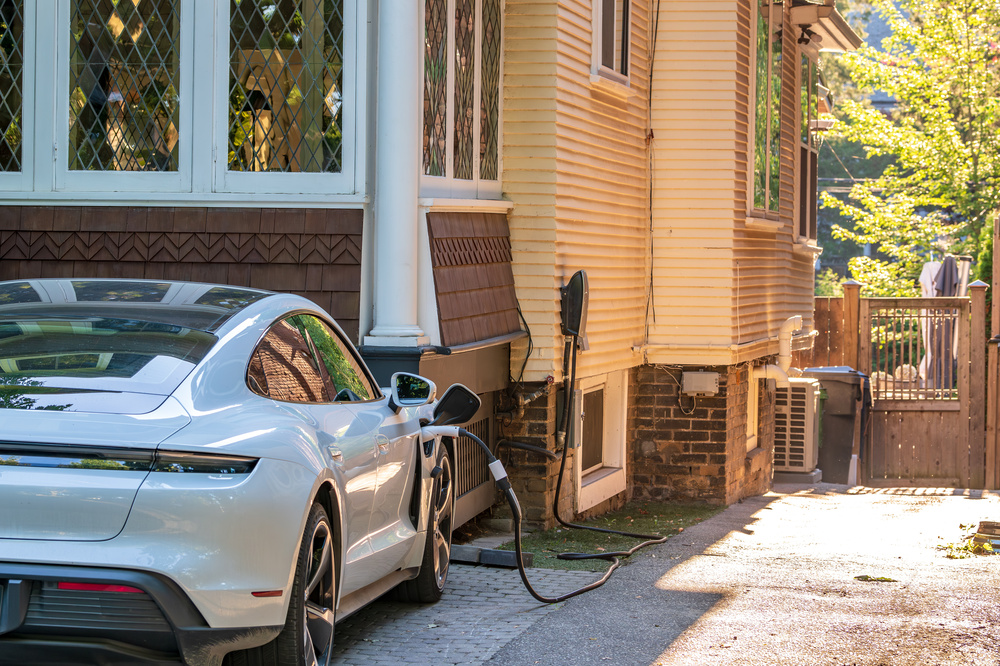 Close up of a high-performance electric vehicle connected to a home charging station in a residential driveway.