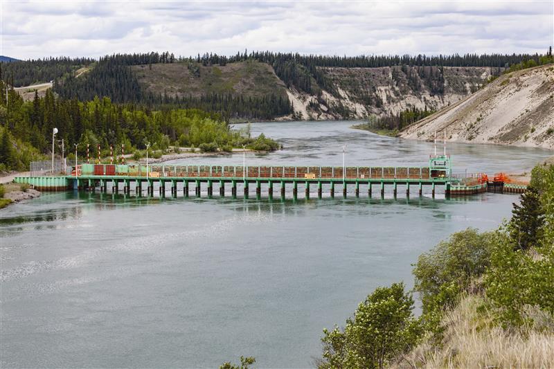 The bright green and red Lewes River Control Structure on Yukon River near Whitehorse on a cloudy summer day.