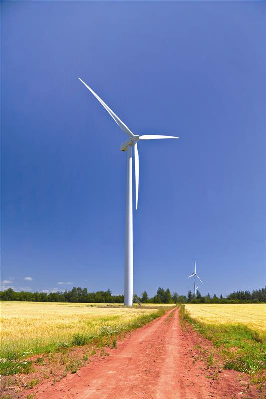 A white wind turbine against deep blue sky in a field with red gravel road on Price Edward Island.