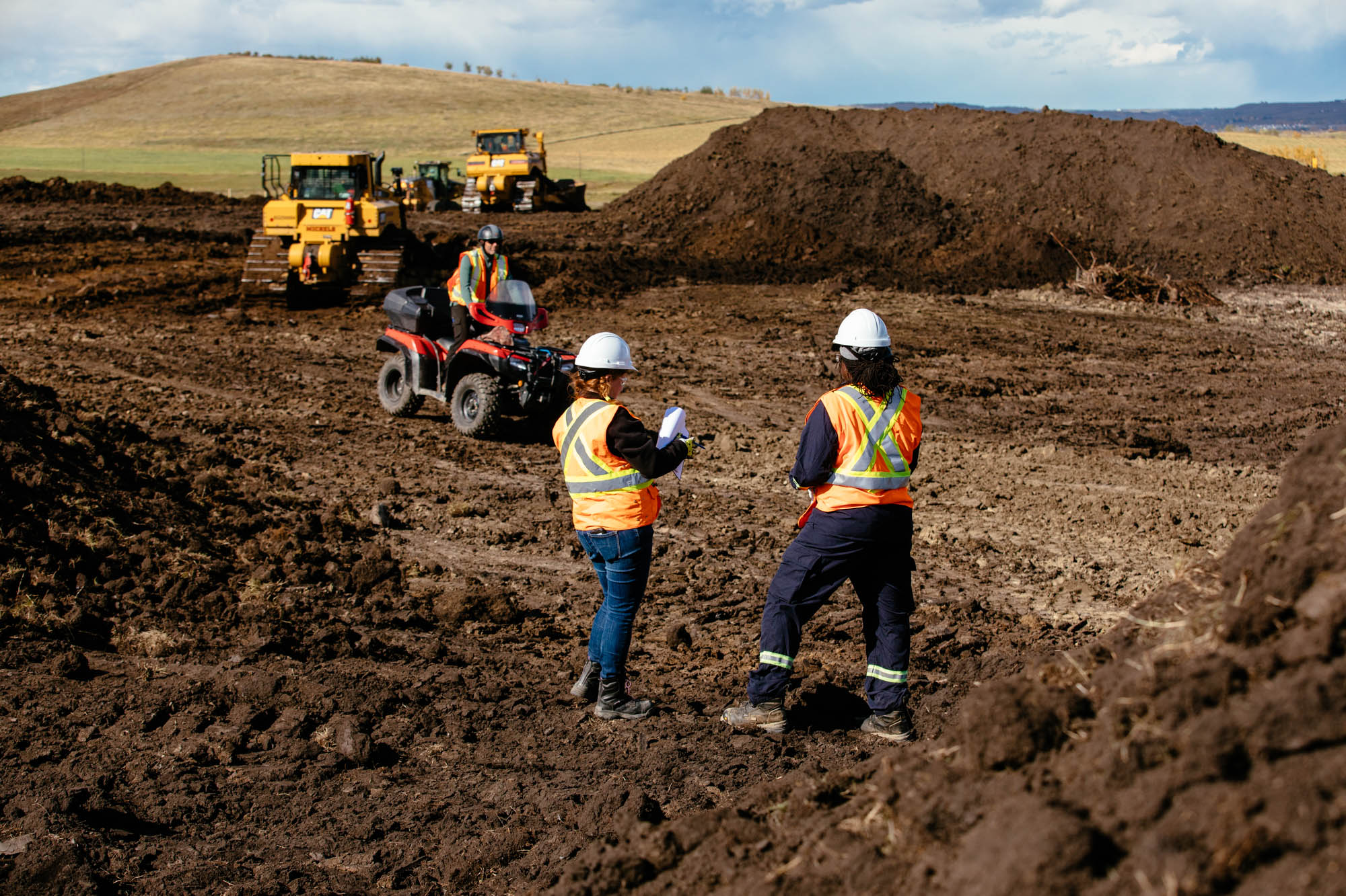 Two CER Inspection Officers on construction site, with worker on ATV and heavy equipment and dirt in the background.