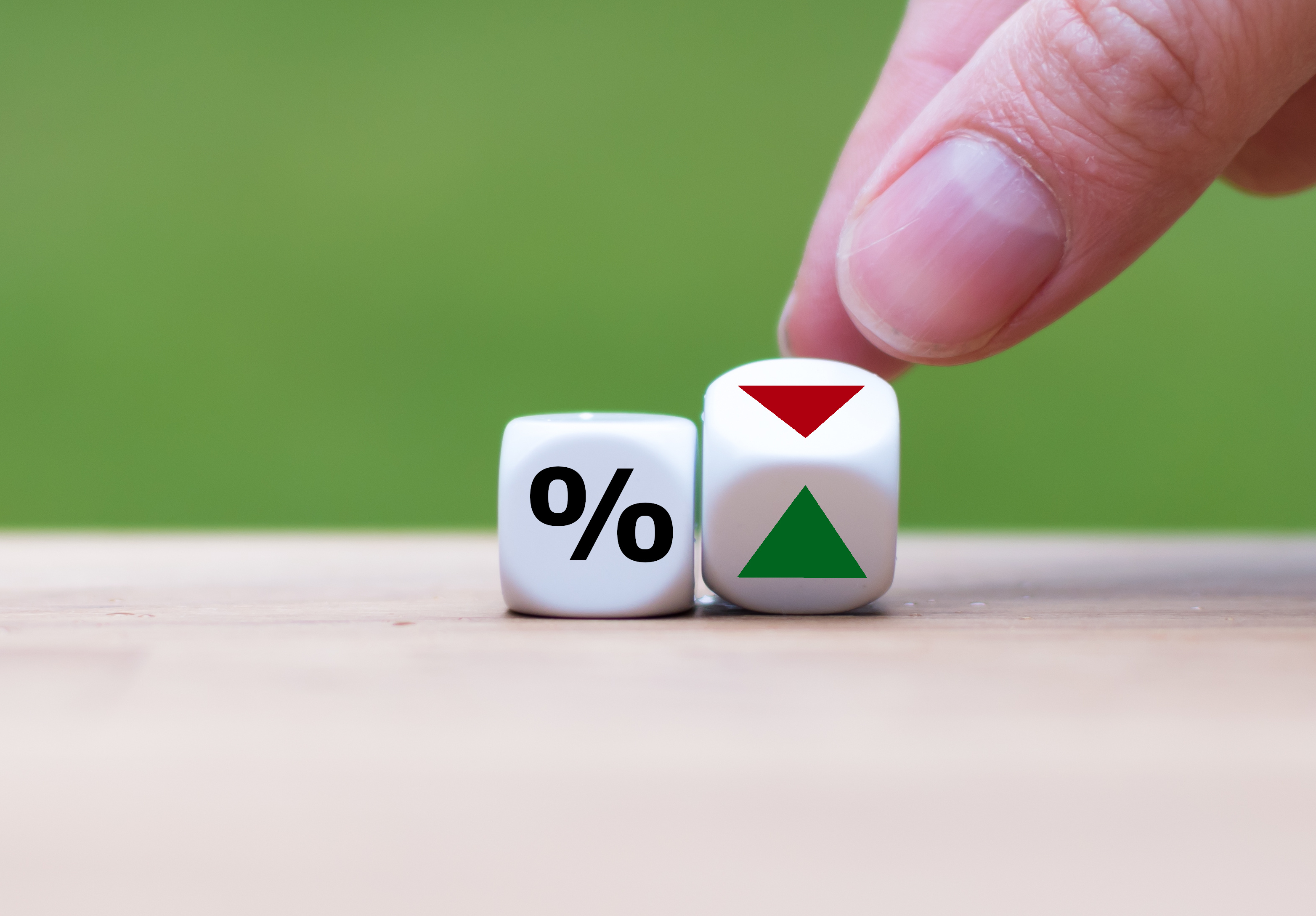 Hand moving two dice, one with percentage sign and other with a red and green arrow.