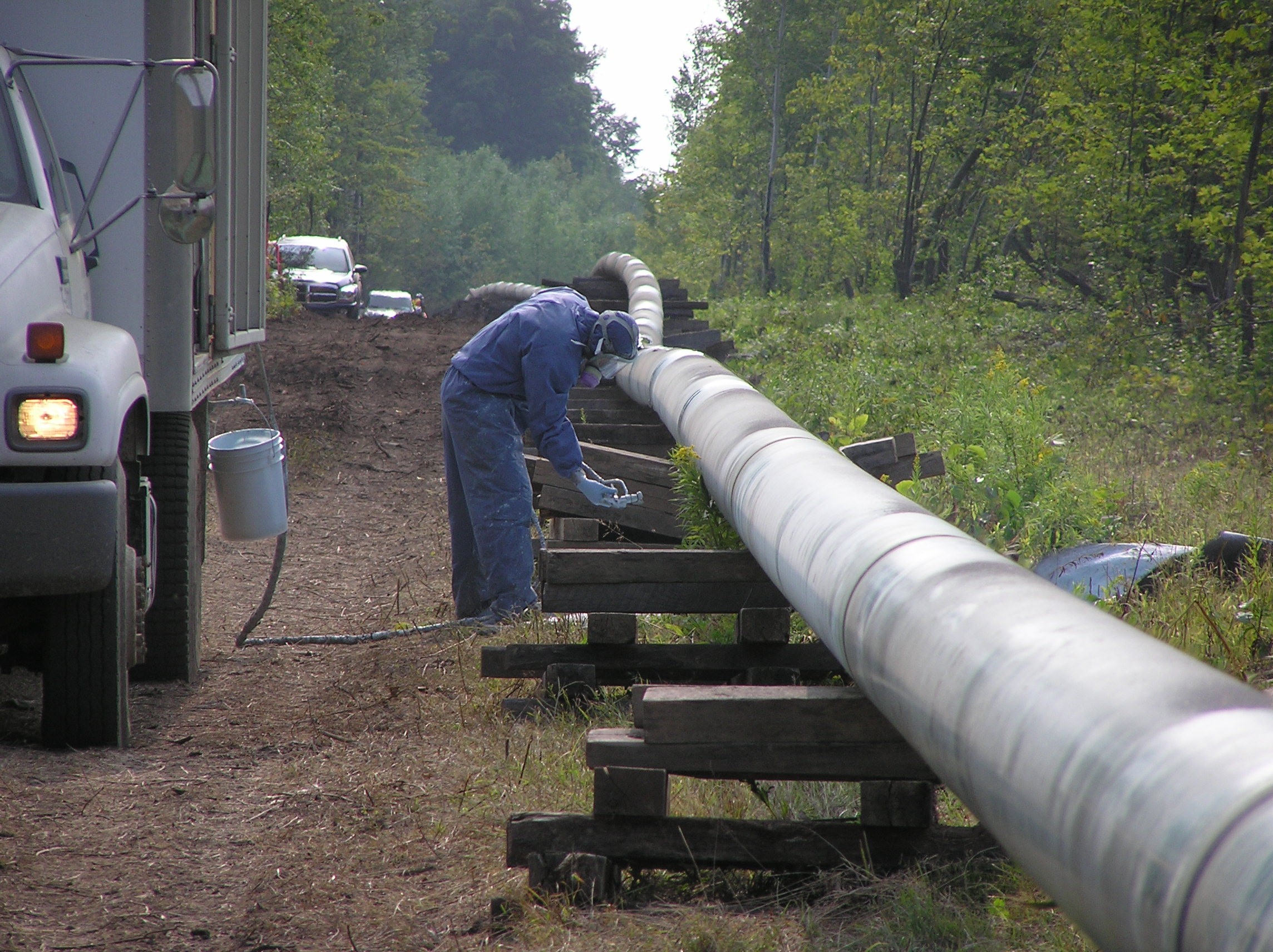 Worker wearing gas mask and inspecting pipeline next to truck.