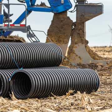 Black corrugated water drainage pipe, field tile, in farm field with tile plow or ditcher in background