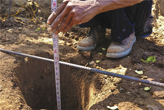 Travailleur mesurant la profondeur d’un trou dans la terre.