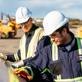 Two people, one a CER inspectors and the other technical staff, look at and run their hands along a pipe. They are there to verify that a company is complying with regulations.