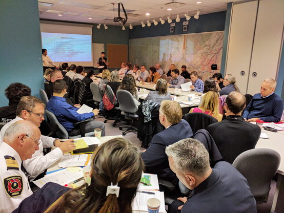 About 30 people from different agencies sitting down in a conference room listening to two people speak. They are there to coordinate a response.