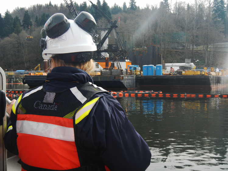 One CER inspector stands with back facing the camera looking at the shoreline where construction of a marine terminal is happening.